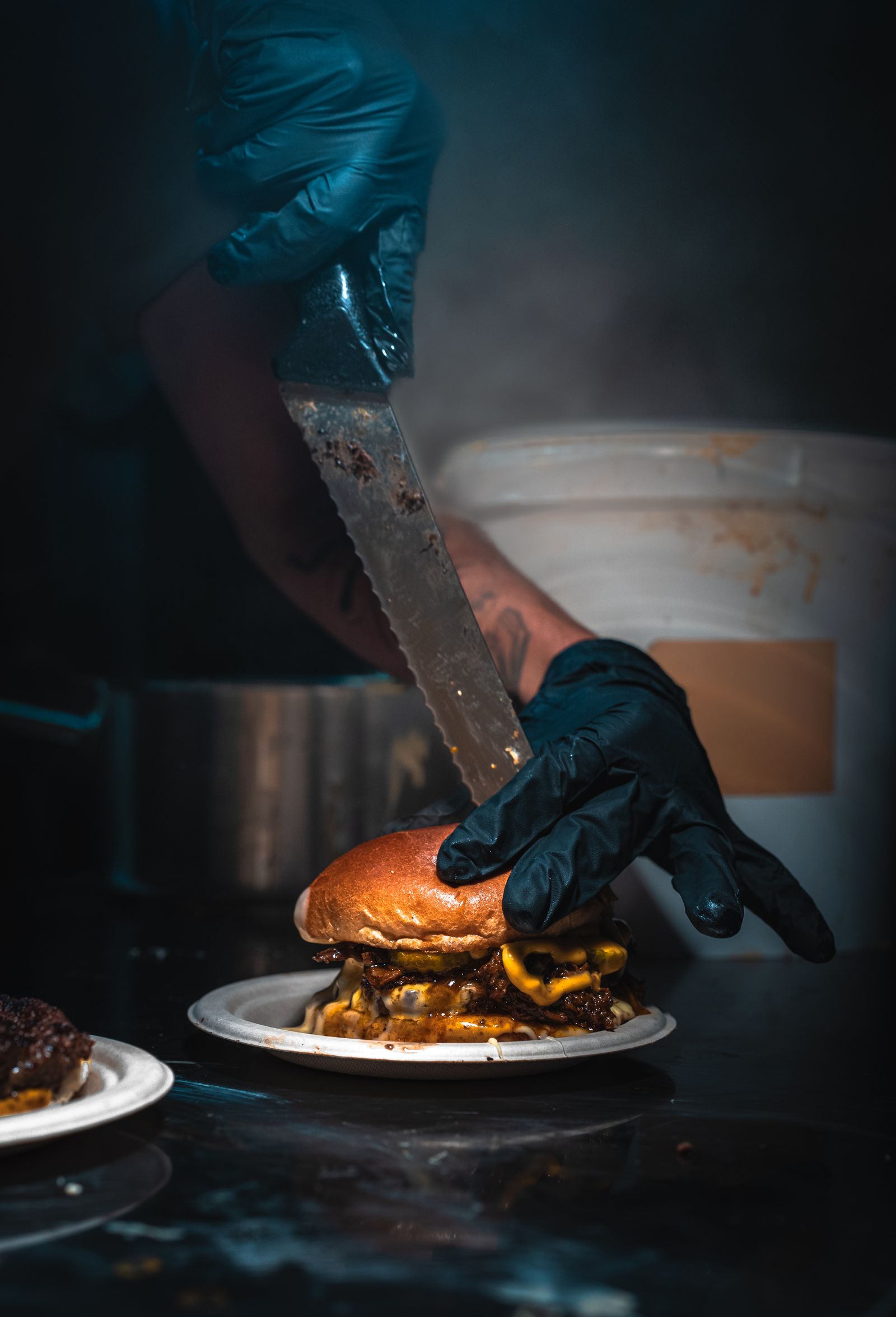 gloved hands slicing a burger during food preparation.