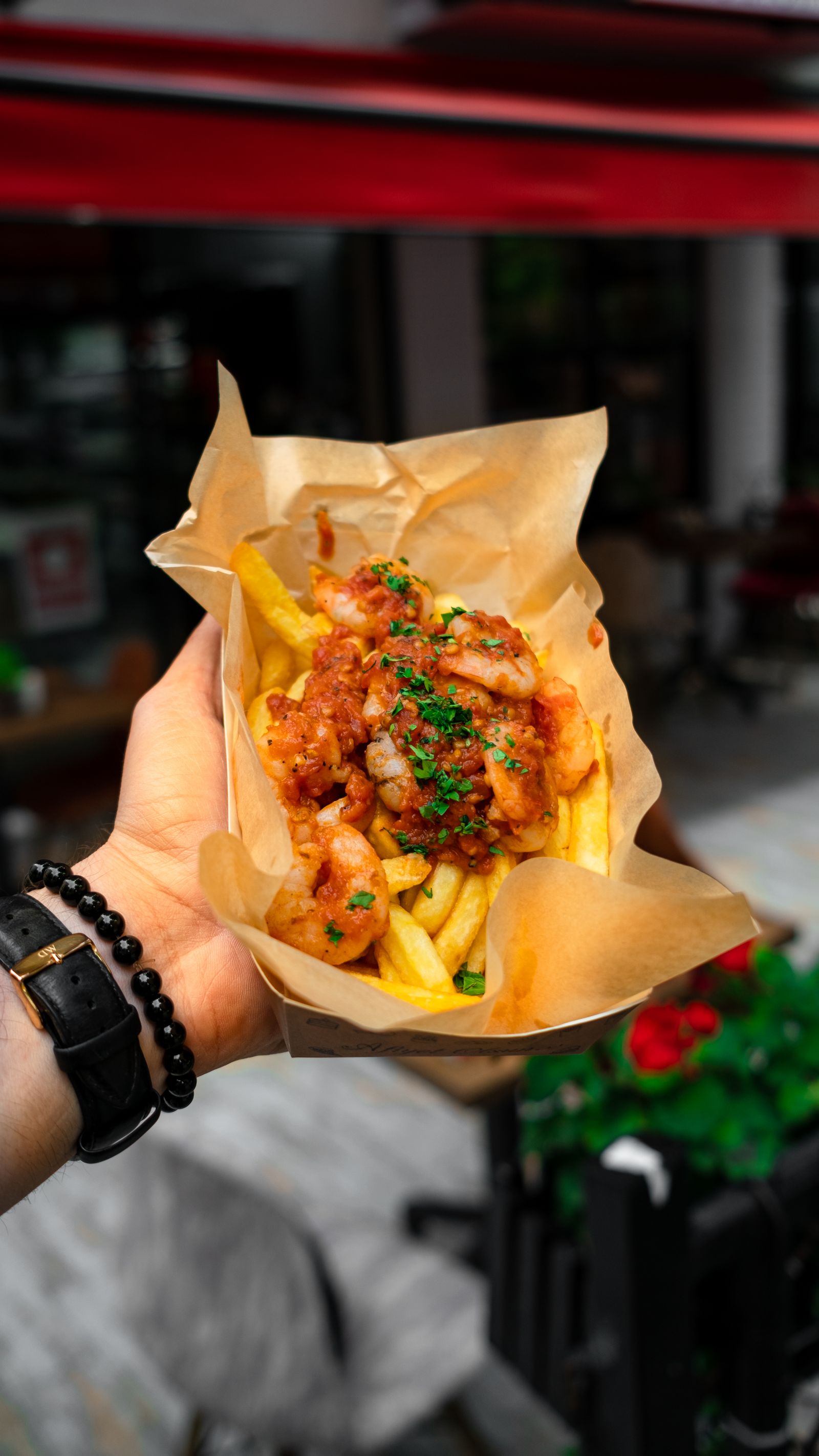 a hand holding loaded fries in a casual street-food setting.