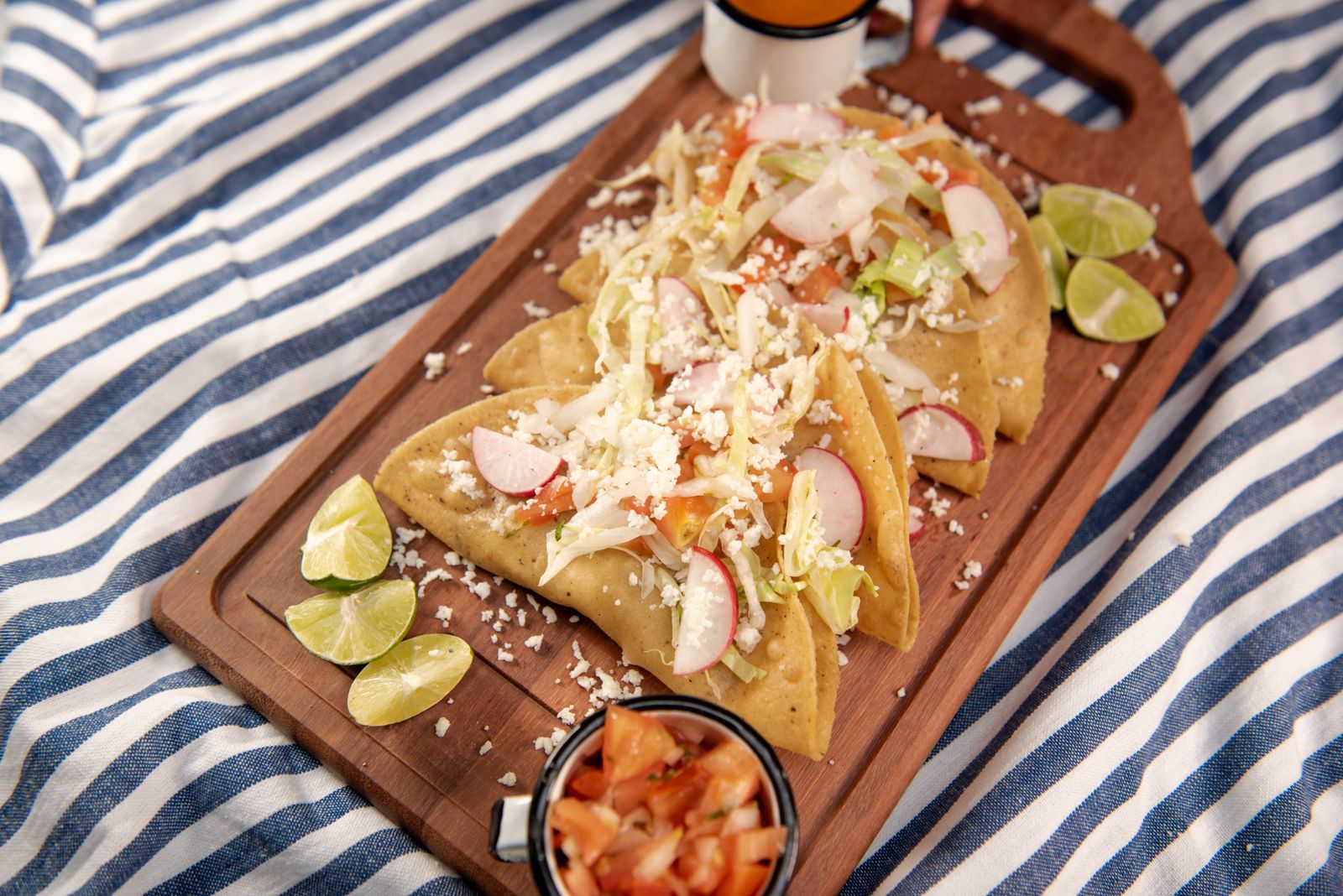 tacos with lime and toppings on a wooden platter.
