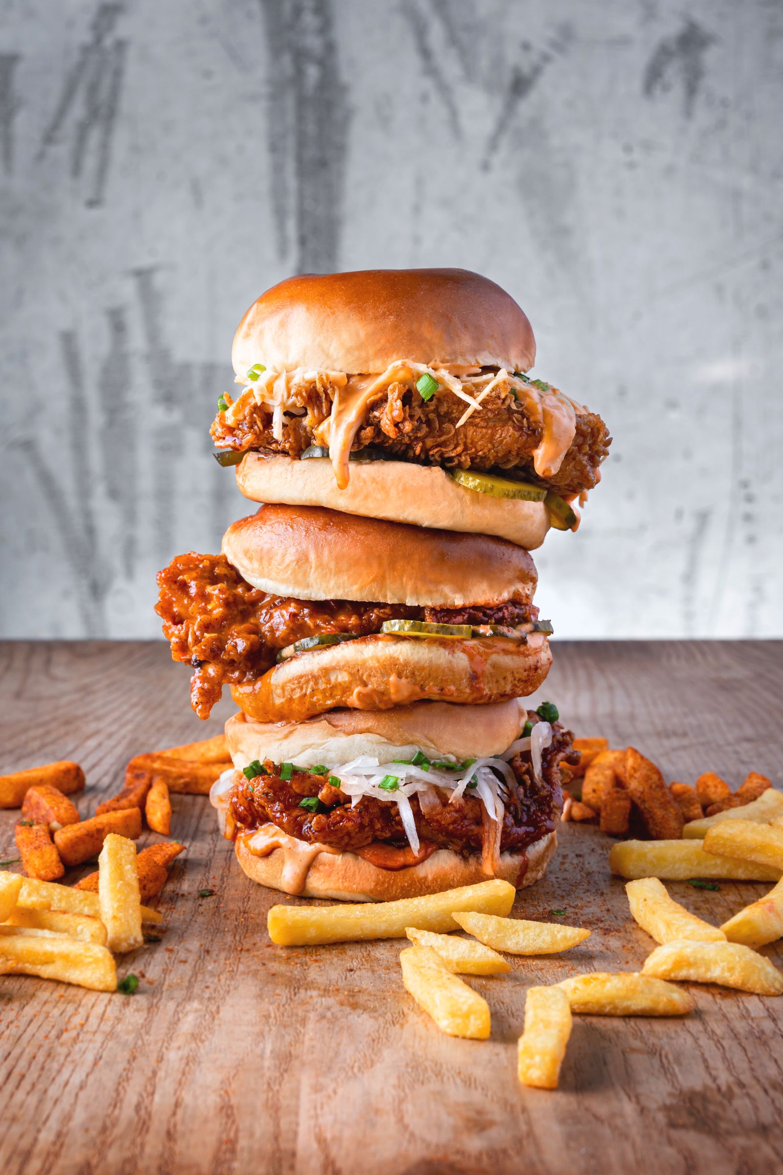 stacked burgers and fries on a rustic wooden table.