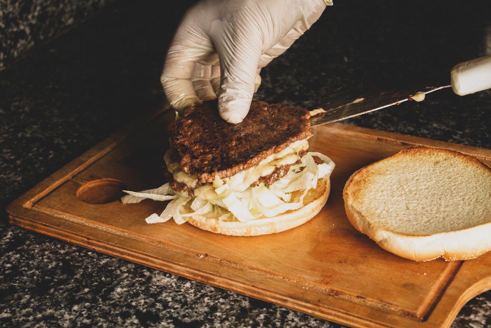 gloved hands assembling a burger in a casual kitchen.
